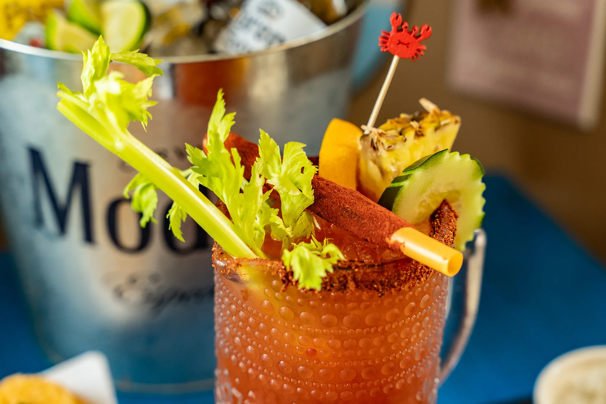 A Wacky Crab Shack Michelada in a chili-rimmed jar garnished with celery, cucumber, pineapple, and a red crab pick