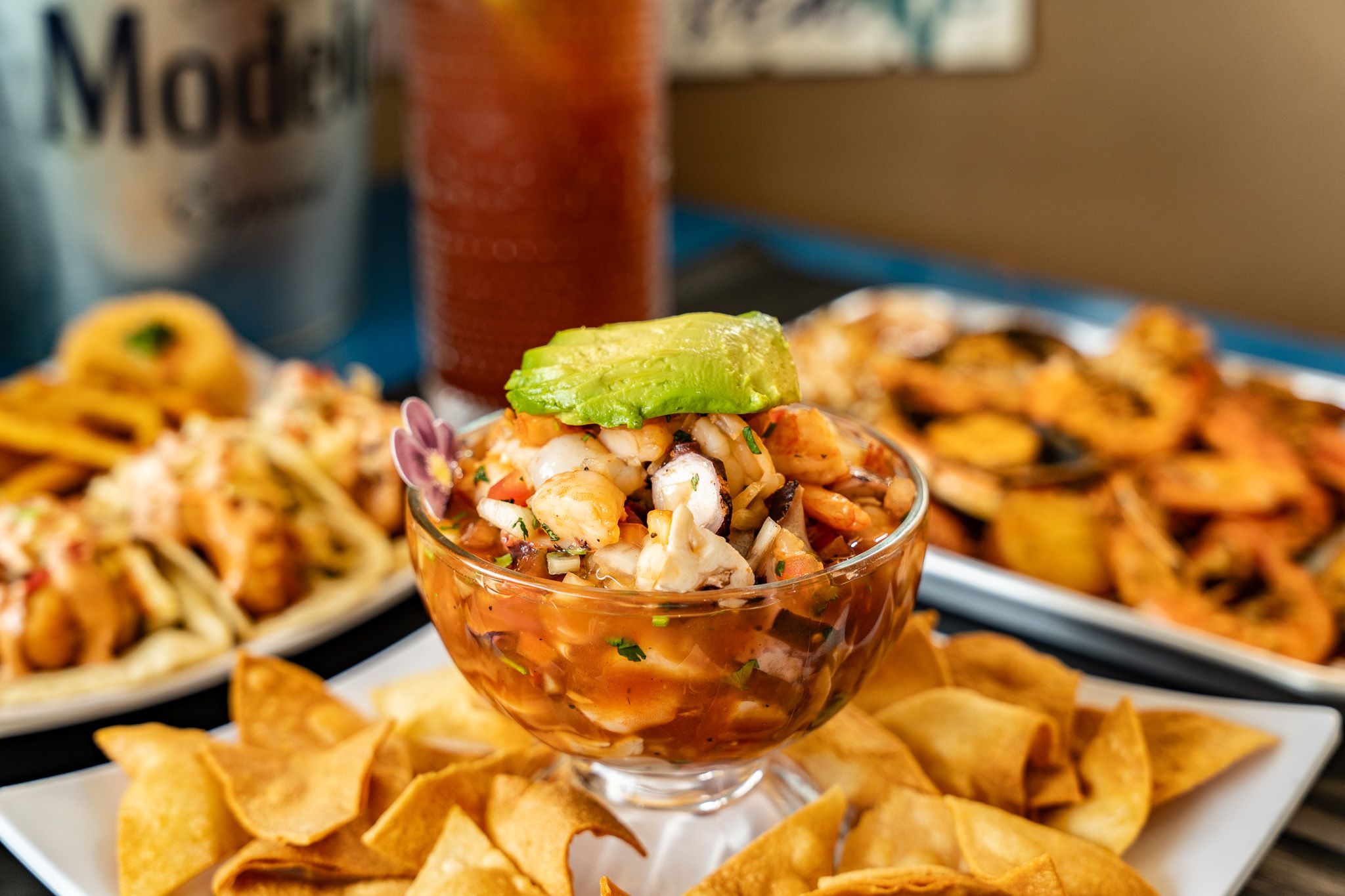 Close-up of Wacky Crab Shack shrimp ceviche topped with avocado, sitting on a bed of tortilla chips with a Michelada behind it